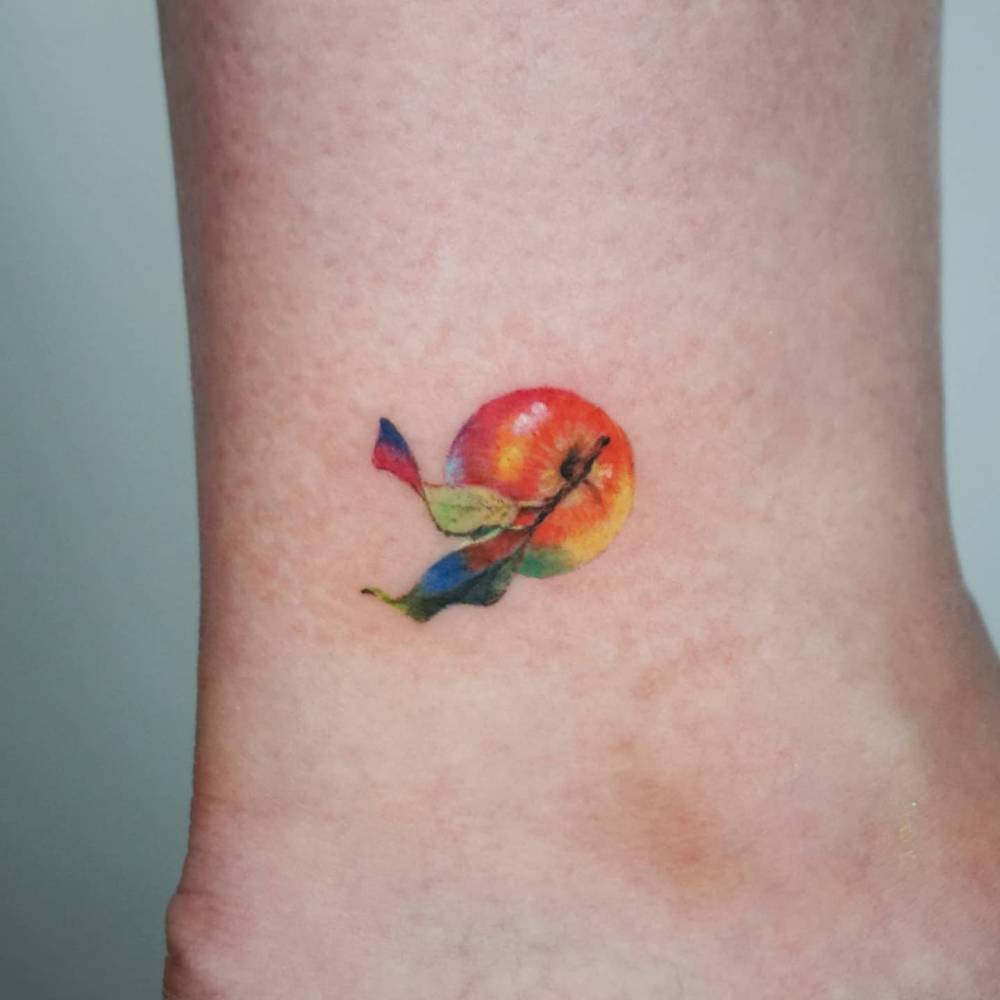 Micro-realistic style apple tattoo located on the ankle.