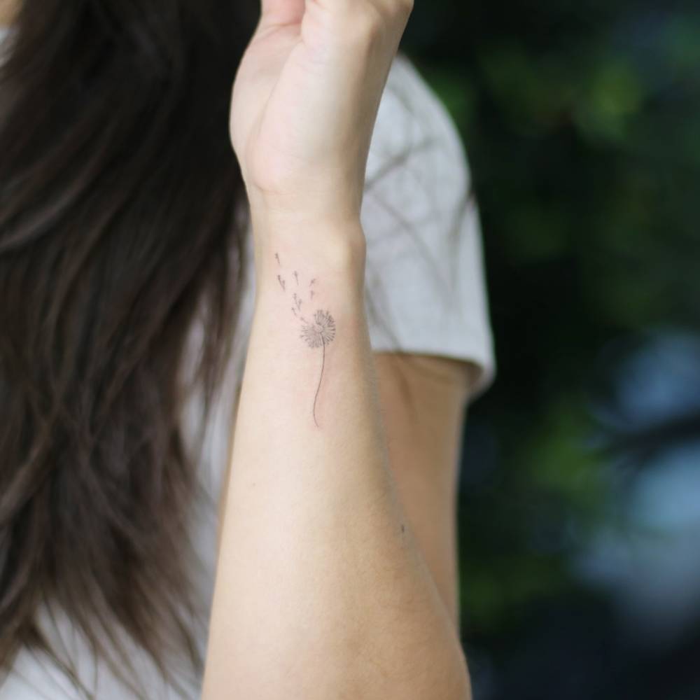 Fine line style dandelion tattoo located on the wrist.