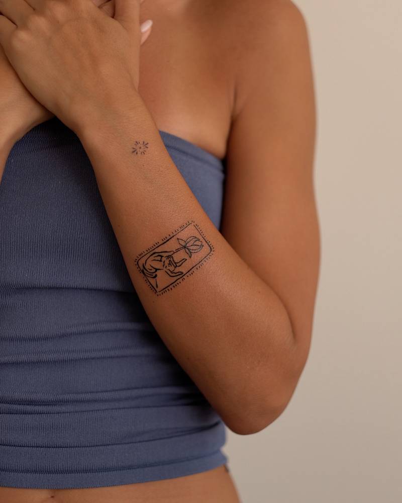 Hand holding flower tattoo located on the forearm.