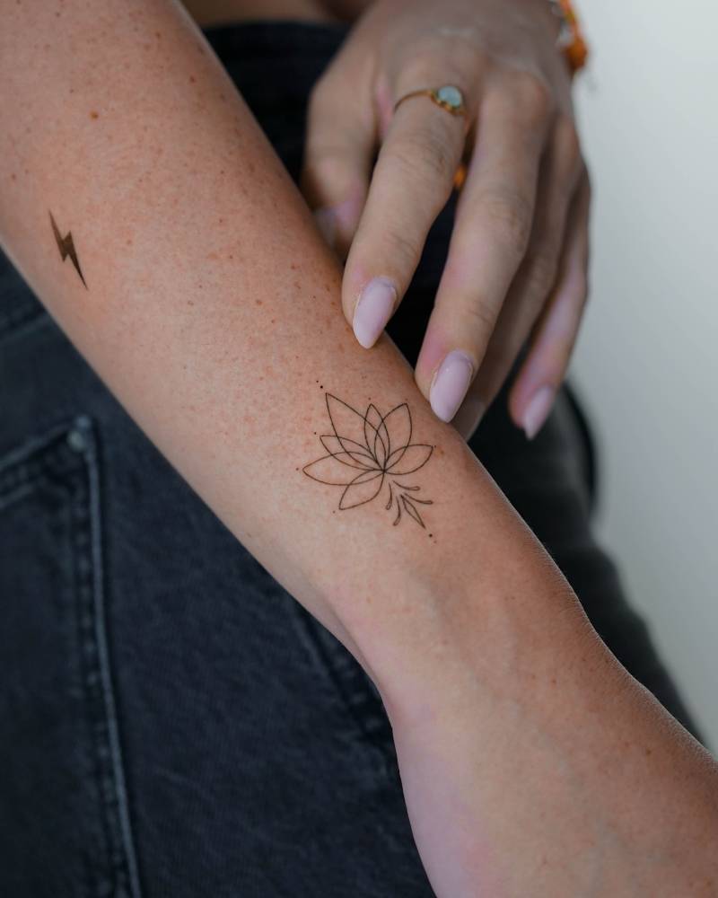 Fine line style lotus flower tattoo located on the wrist.