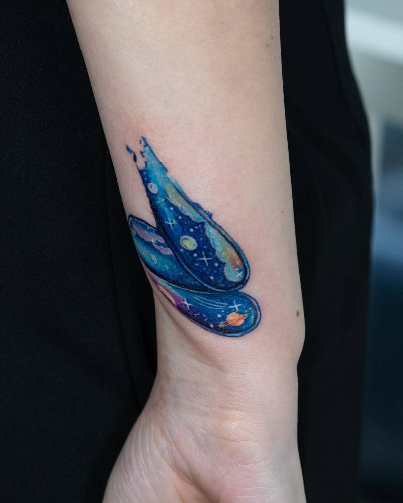 Watercolor style brush strokes and galaxies tattoo located on the wrist.