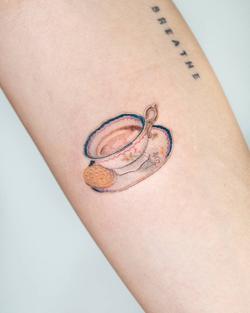 Tea and biscuit tattoo in watercolor style located on the inner forearm.