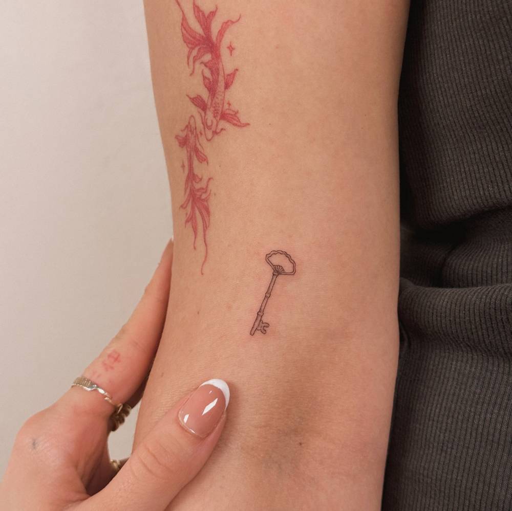 Fine line style key tattoo located on the bicep.