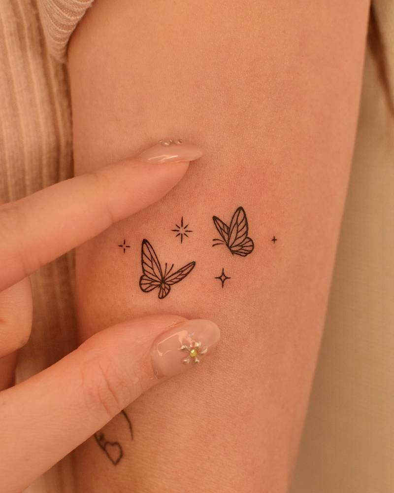 Fine line style butterfly couple and sparkling stars tattoo.