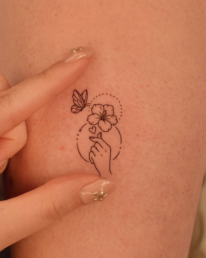 Korean finger heart, butterfly and hibiscus tattoo located on the upper arm.