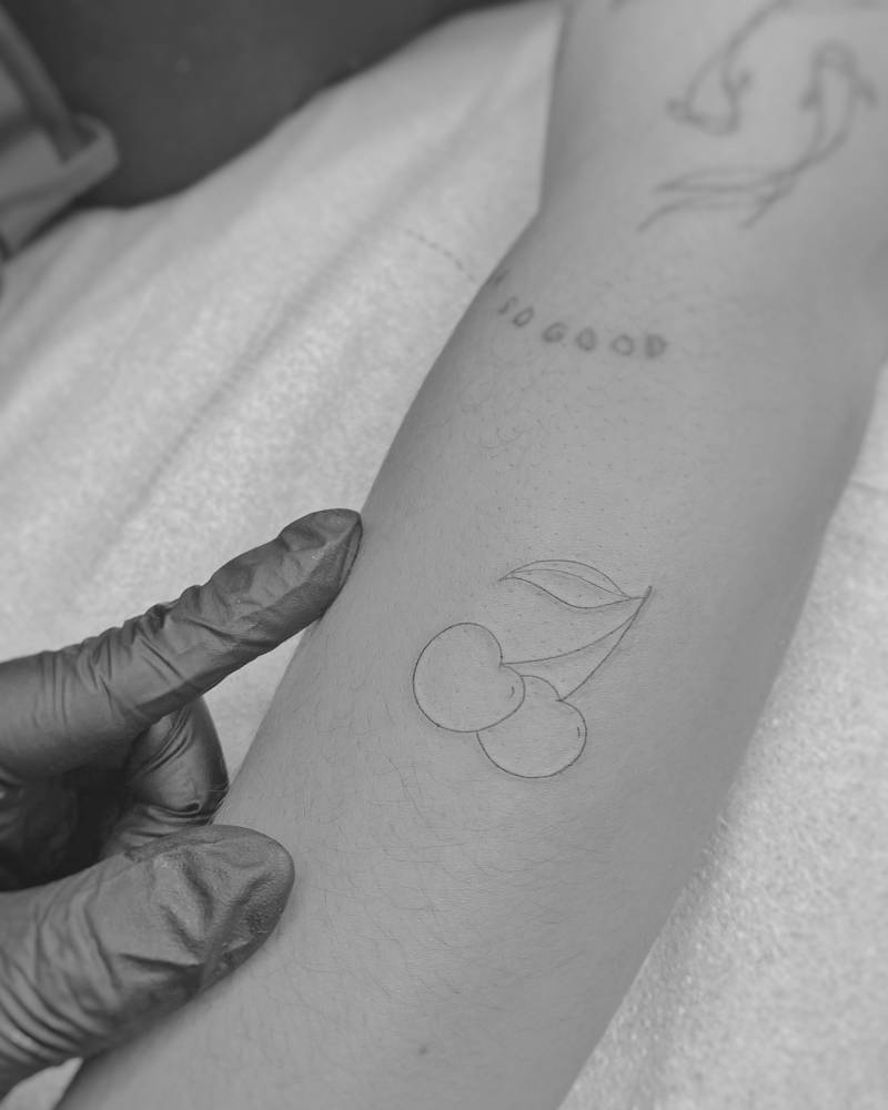 Fine line style cherries tattooed on the forearm.