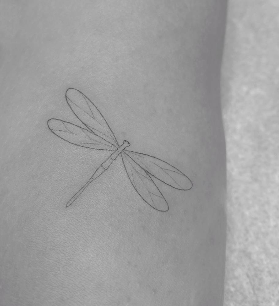 Fine line style dragonfly tattoo located on the upper arm.