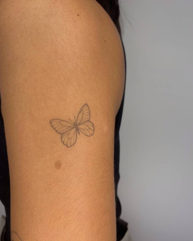 Little butterfly tattoo in fine line style located on the upper arm.