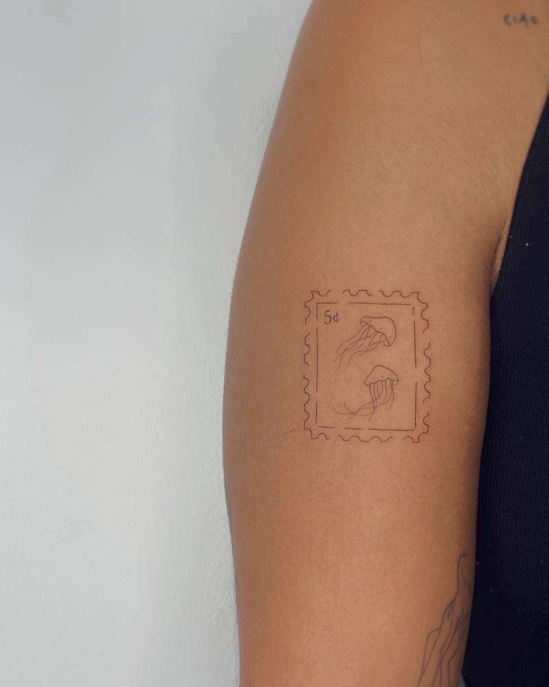 Fine line style jellyfish stamp tattoo located on the upper arm.