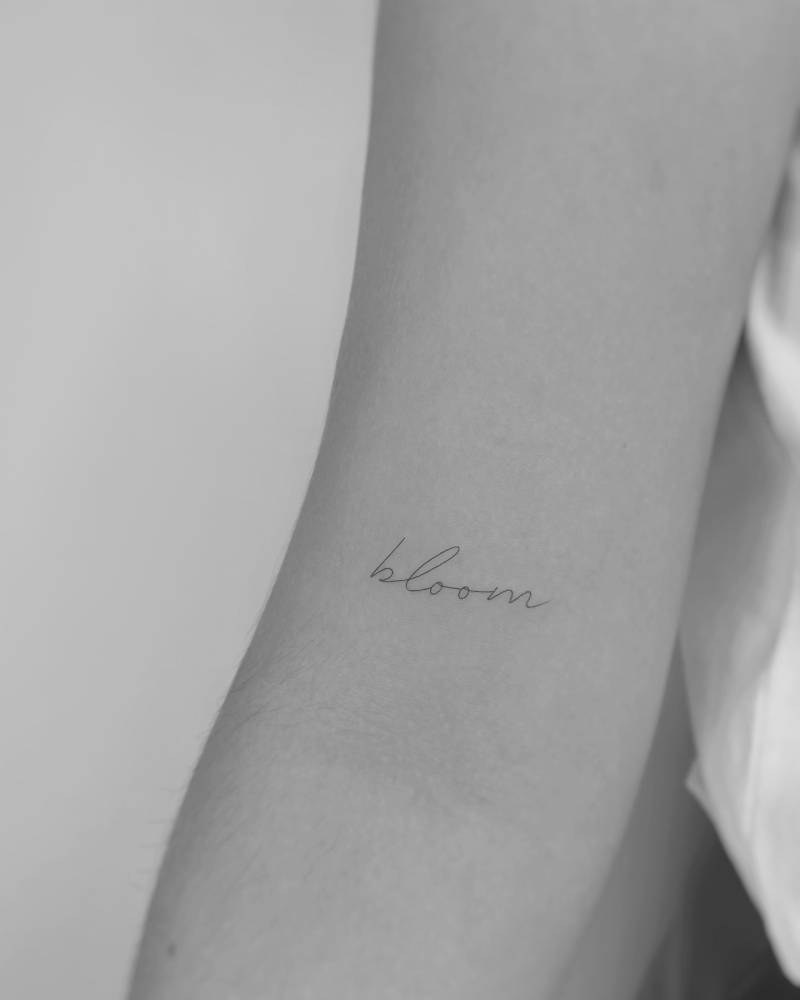 Lettering tattoo of the word "bloom" placed on the bicep.
