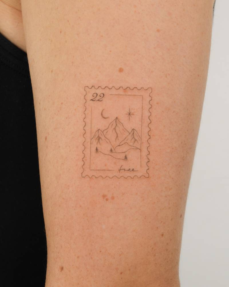 Fine line style mountain stamp tattoo located on the upper arm.