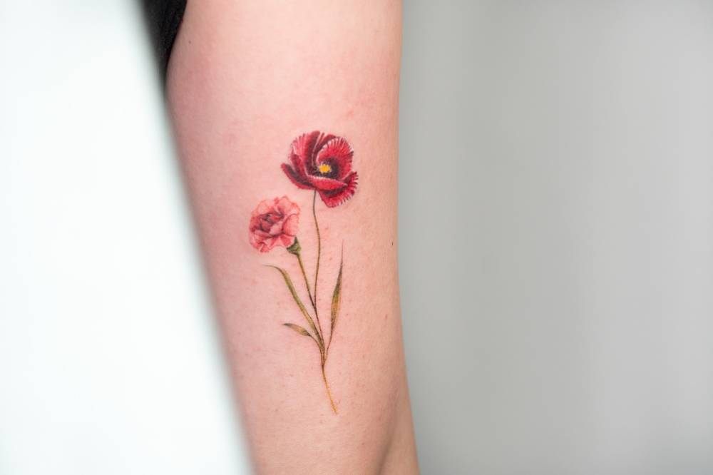 Carnation and poppy flower tattoo in micro-realistic style located on the tricep.