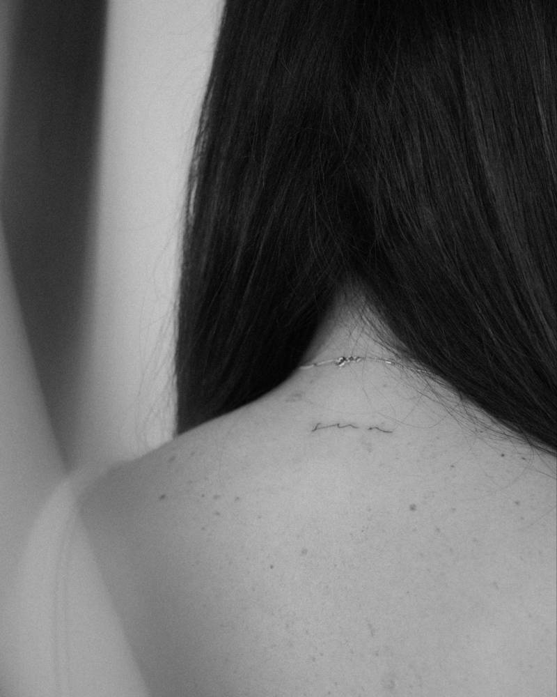 Handwritten lettering tattoo of the word "sun" located on the upper back.