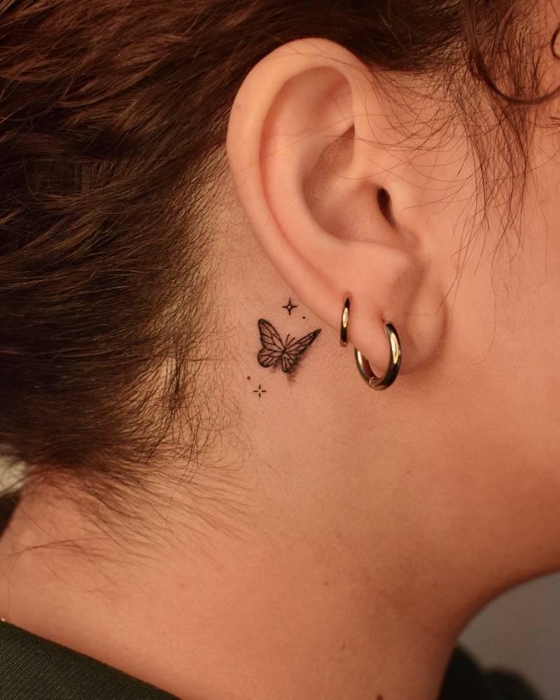 Little butterfly and sparkling stars tattoo located behind the ear.