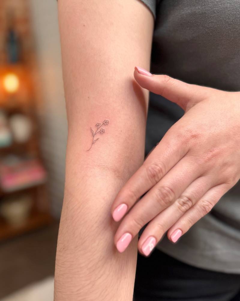 Tiny minimalistic cherry blossom tattoo located on the upper arm.