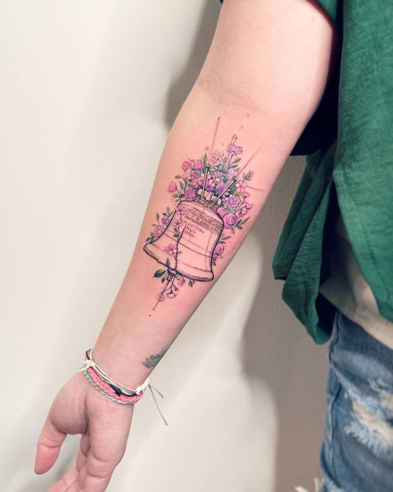 Liberty Bell tattoo in watercolor style located on the inner forearm.