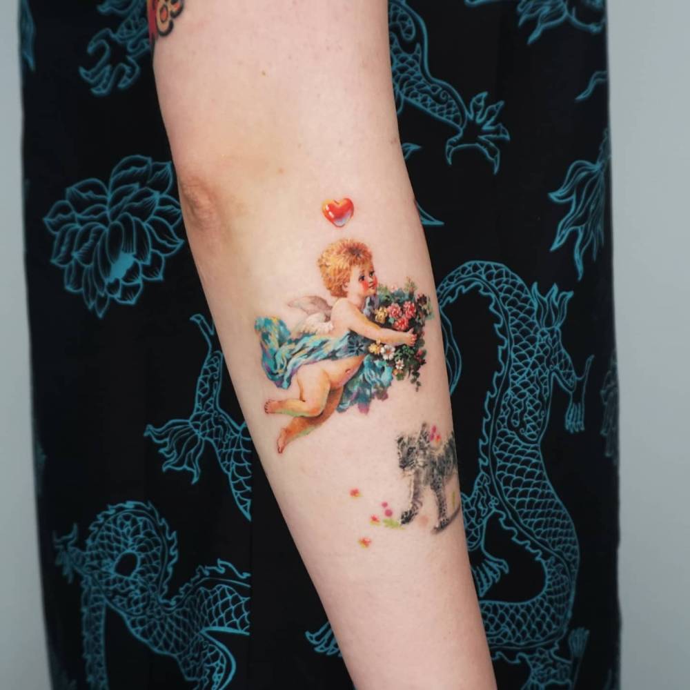 Realistic style cherub tattoo located on the forearm.
