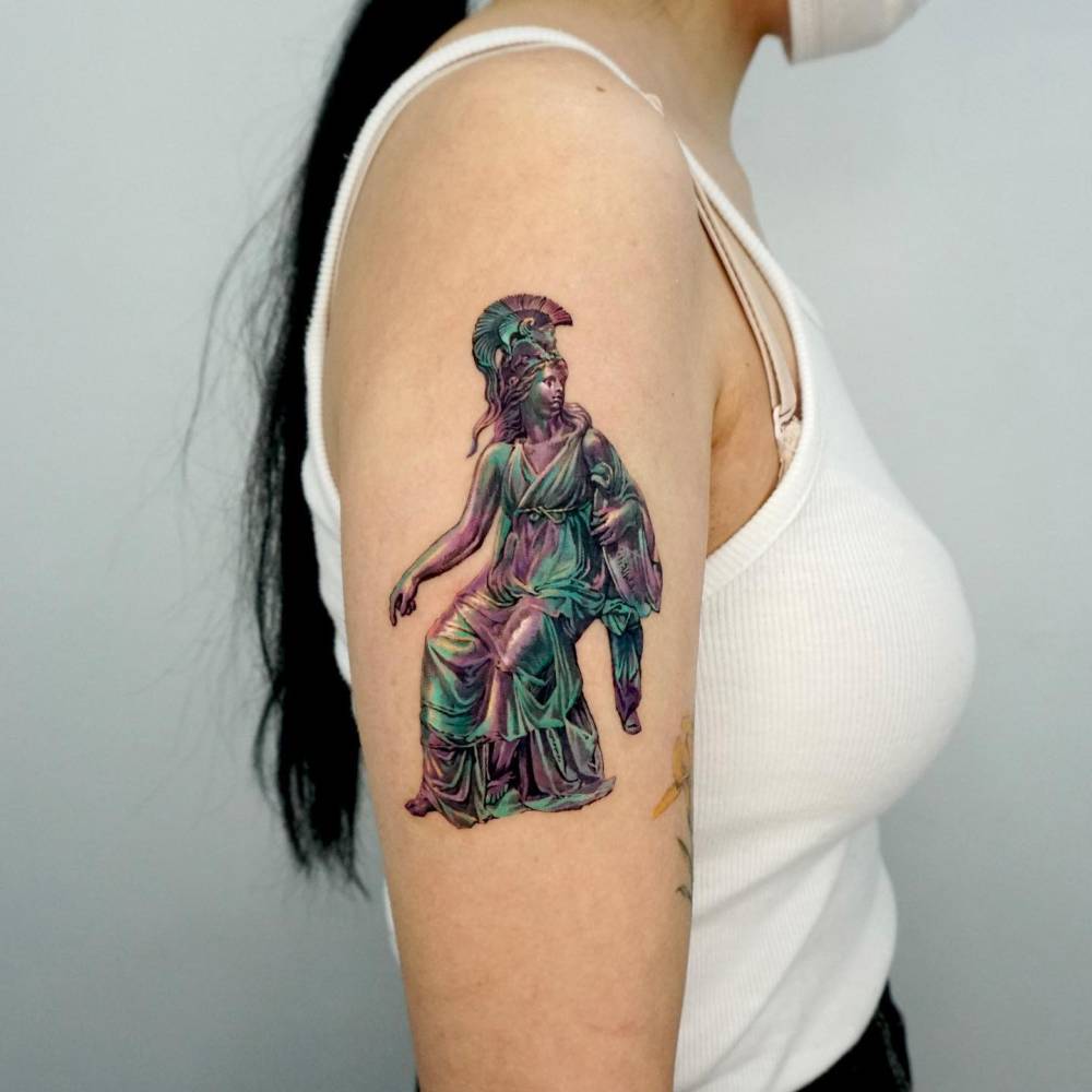Athena sculpture tattoo in realistic style located on the upper arm.