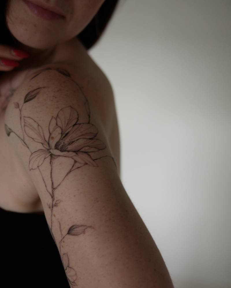 Magnolia flower tattoo in illustrative style placed on the upper arm.