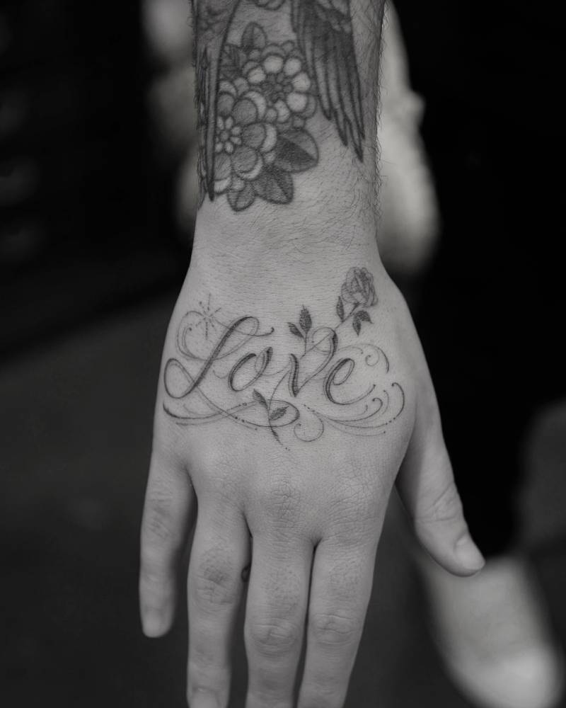 Word "love" and rose tattoo located on the hand.