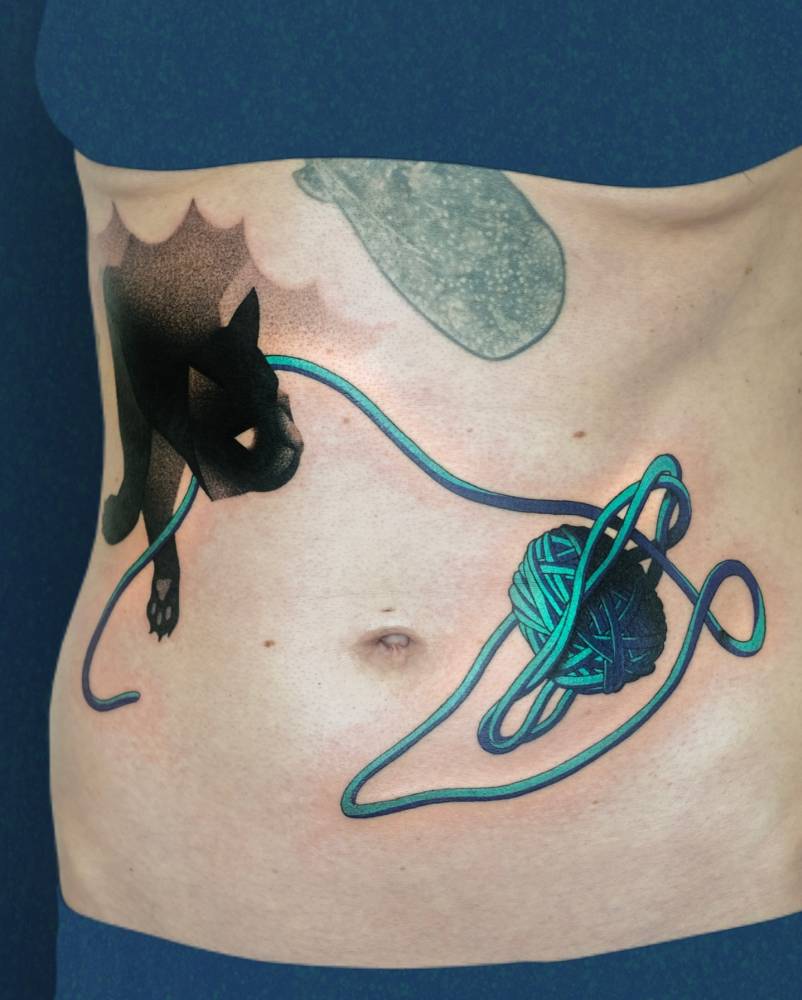 Black cat and wool yarn tattoo located on the stomach.