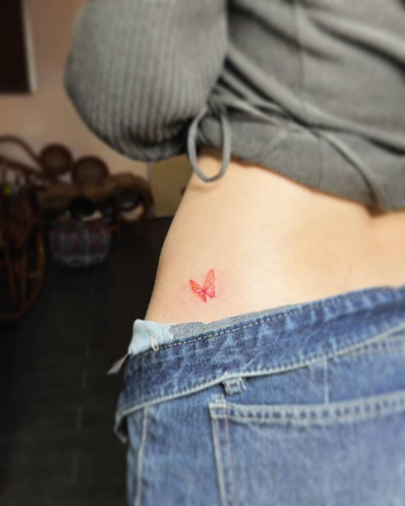 Red butterfly tattoo placed on the hip, done in illustrative style.