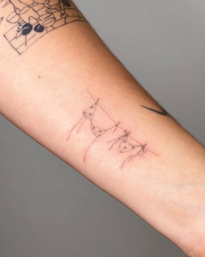 Fine line style bikini and clothes line tattoo located on the wrist.