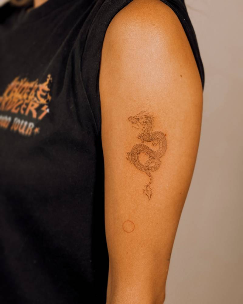 Fine line style dragon tattoo located on the upper arm.