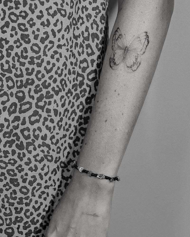 Flying butterfly tattoo located on the forearm, illustrative style.