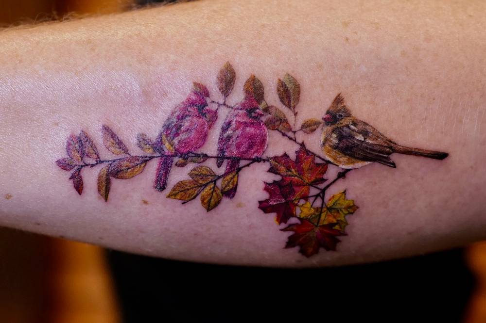 Cardinals on a branch tattooed on the forearm.