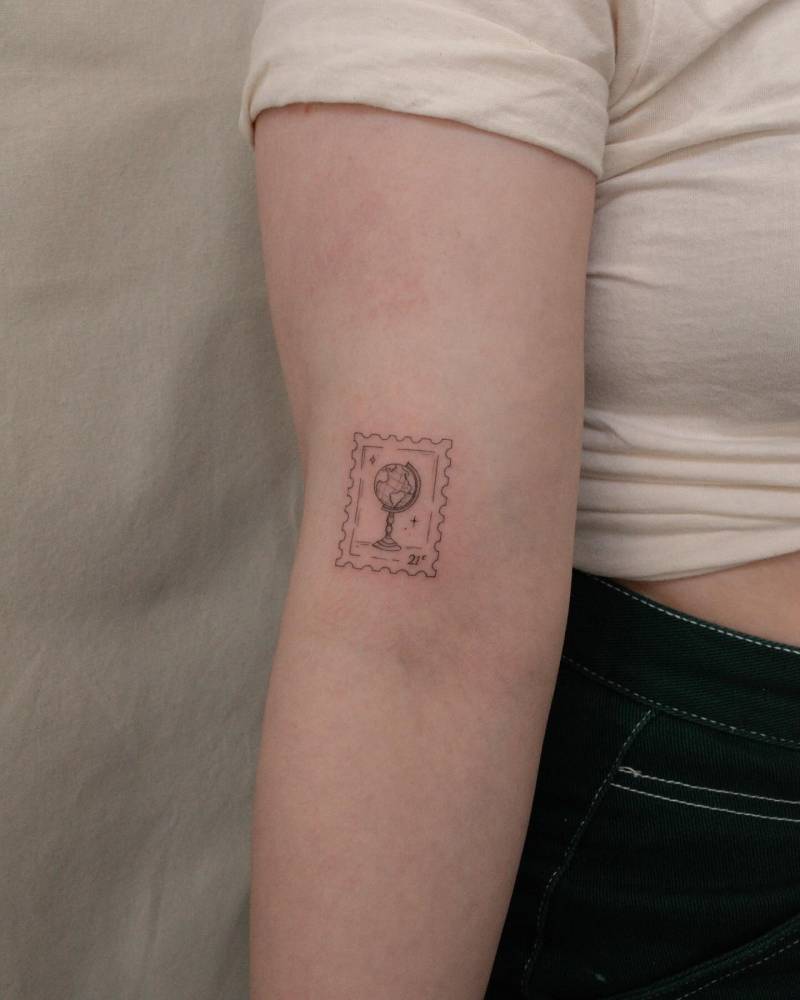 World globe stamp tattoo located on the bicep.