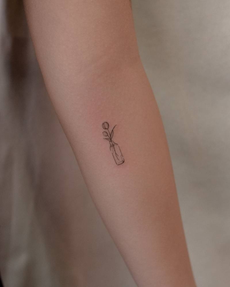 Flower in a bottle tattoo in fine line style done on the inner forearm.
