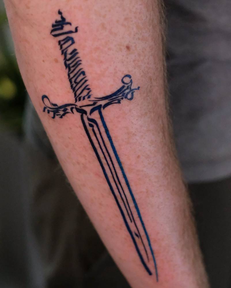 Hebrew lettering dagger tattoo located on the forearm, original design by Gabriel Wolff.
