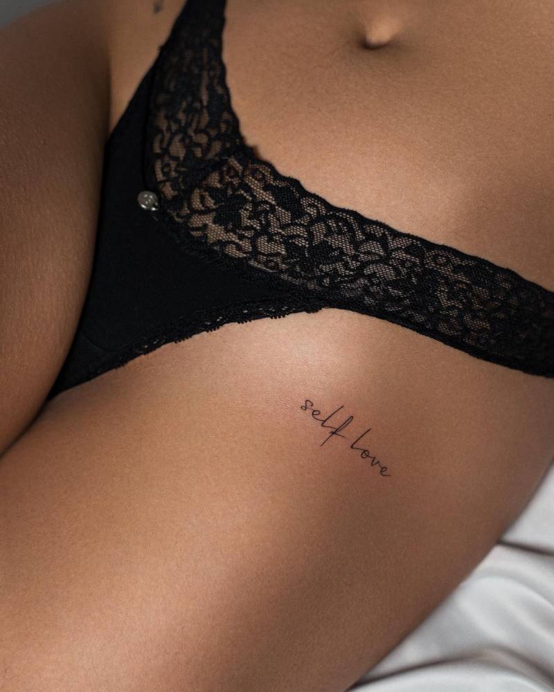 Tattoo that says "self love" handwritten on the hip.