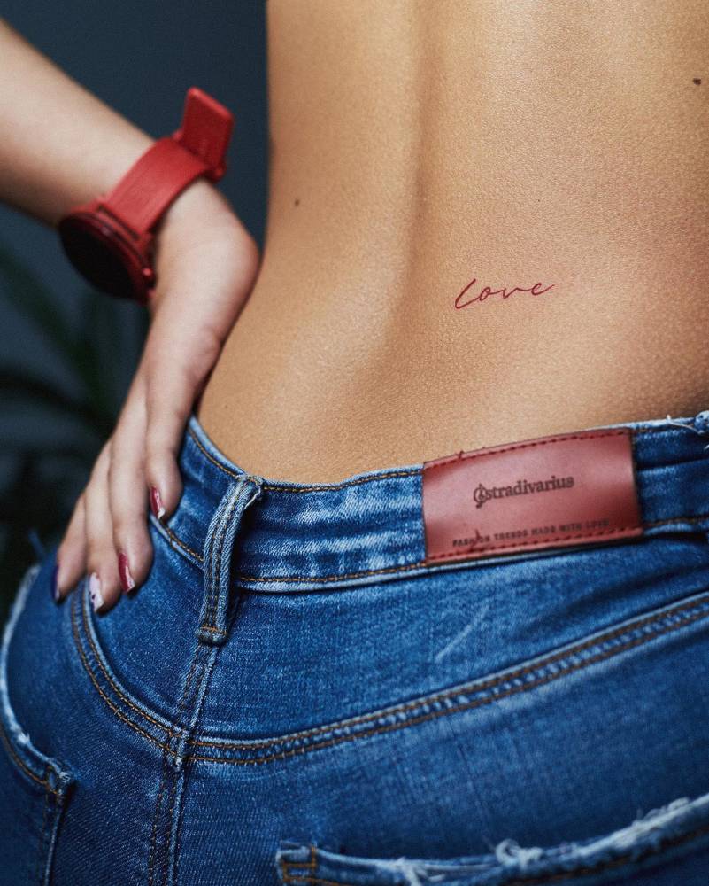 Lettering tattoo of the word "love" in red ink placed on the lower back.