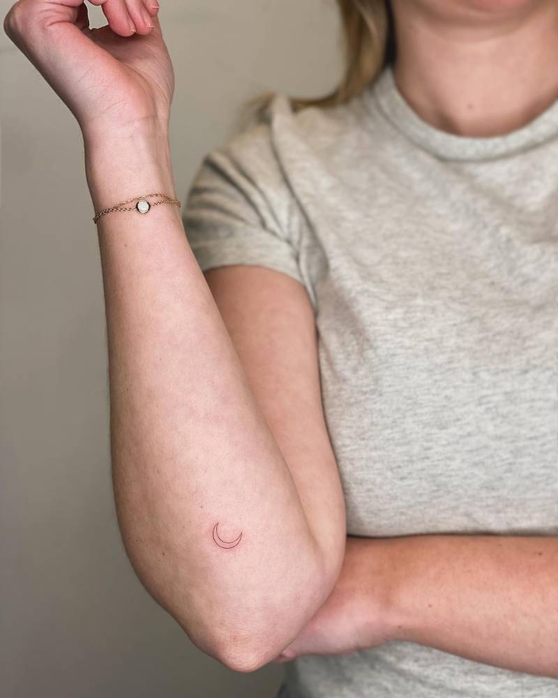 Minimalistic style crescent moon tattoo located on the forearm.