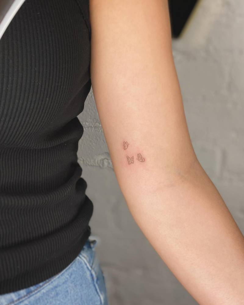 Minimalistic butterflies tattooed on the inner arm, fine line style.