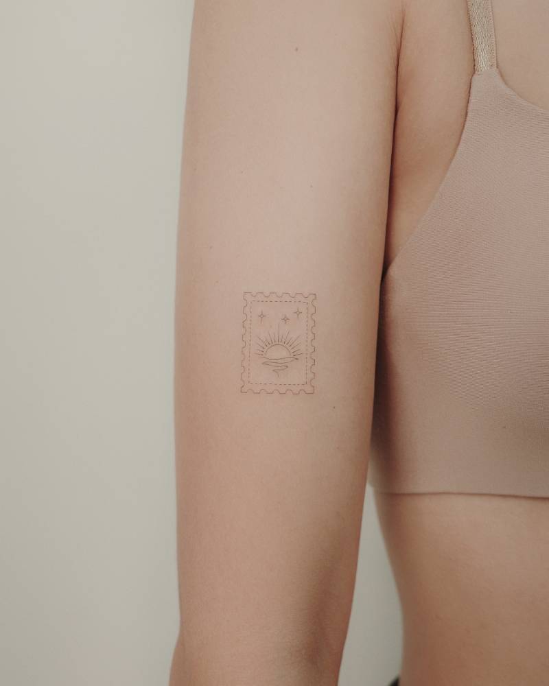 Fine line style sea sunset stamp tattoo placed on the upper arm.