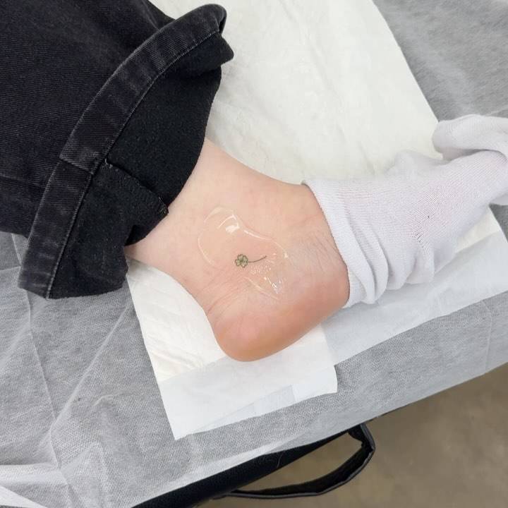 Tiny minimalistic green four leaf clover tattoo located on the ankle.