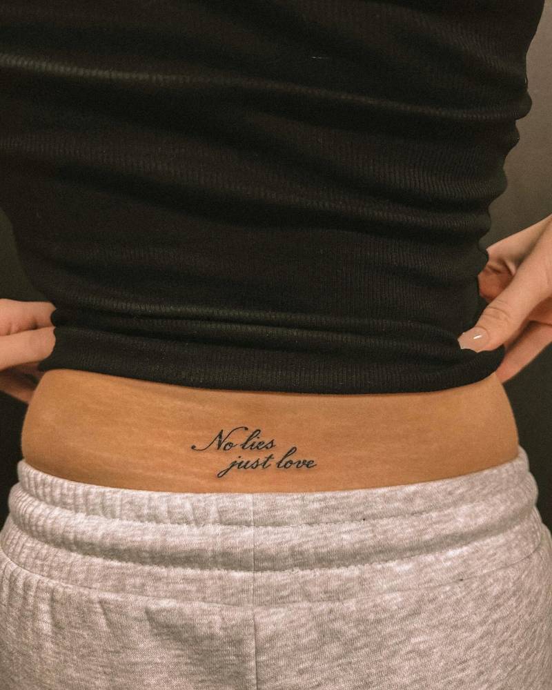 "No lies, just love" lettering tattoo located on the lower back.
