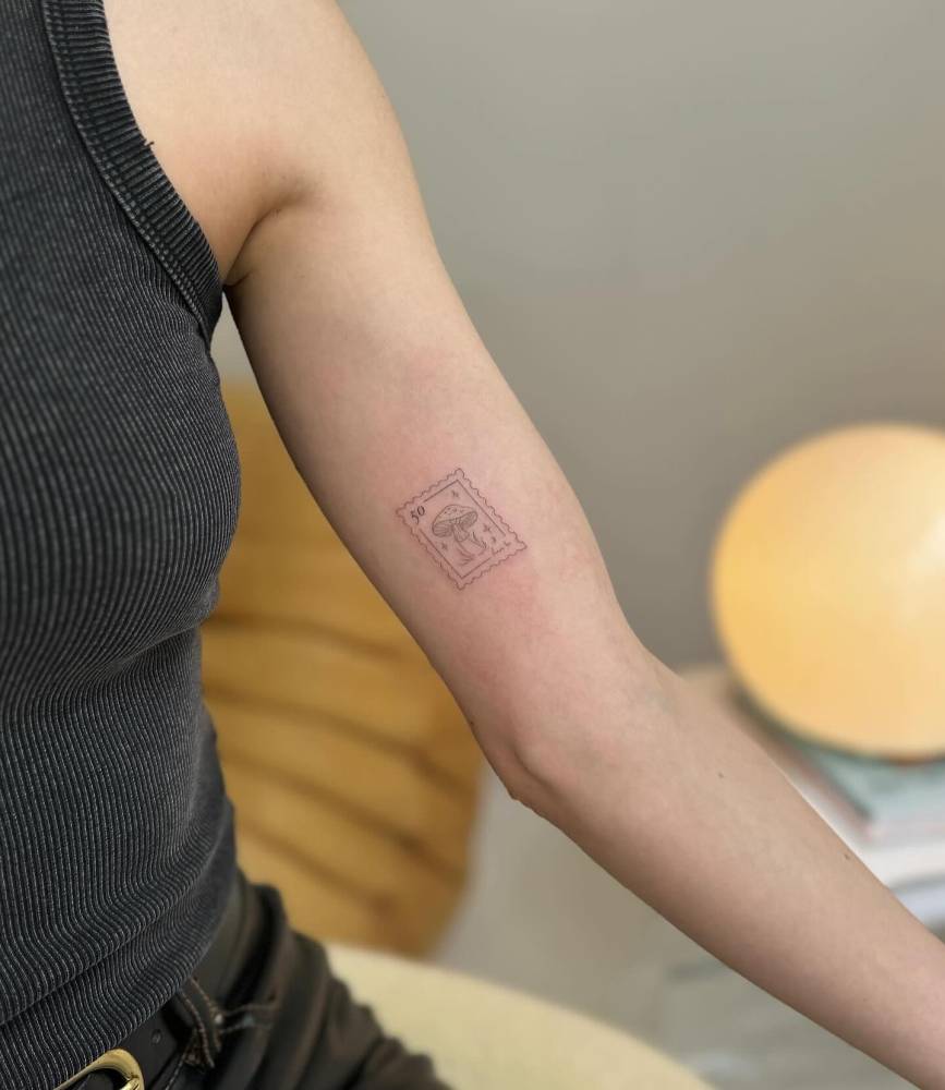 Fine line style mushroom stamp tattoo placed on the inner arm.