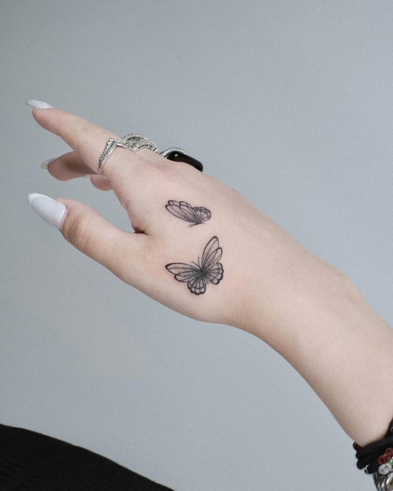 Illustrative style butterfly couple tattoo located on the hand.