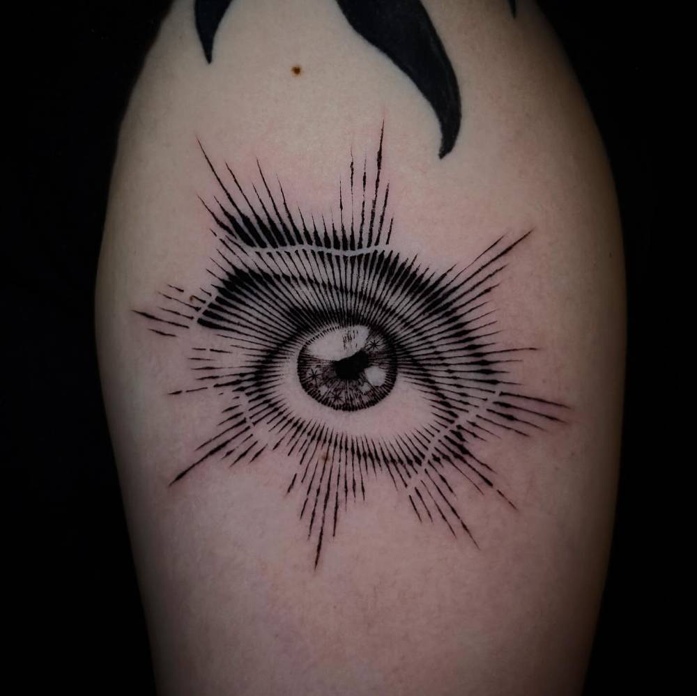 Engraving style eye tattoo located on the upper arm.