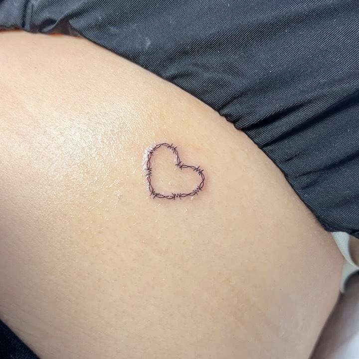 Fine line style barbed wire heart tattoo located on the lower back.