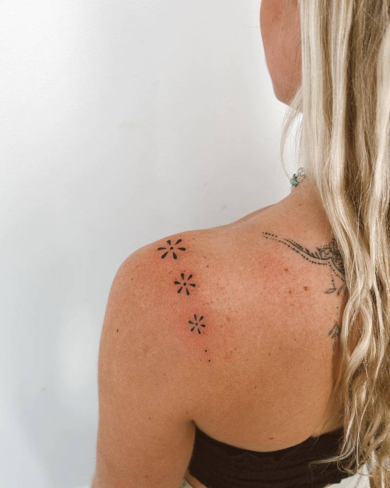 Hand poked flowers tattooed on the shoulder, minimalistic style.