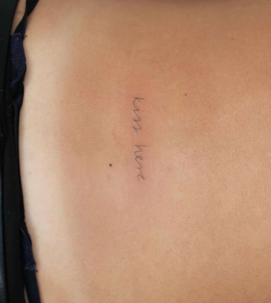 "Kiss here" lettering tattoo located on the lower back.