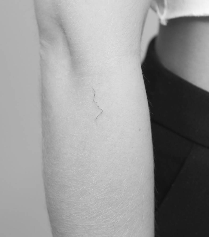 Minimalistic style kiss tattoo located on the forearm.