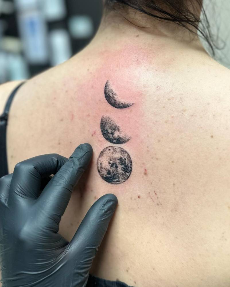 Moon phases tattoo located on the upper back, illustrative style.