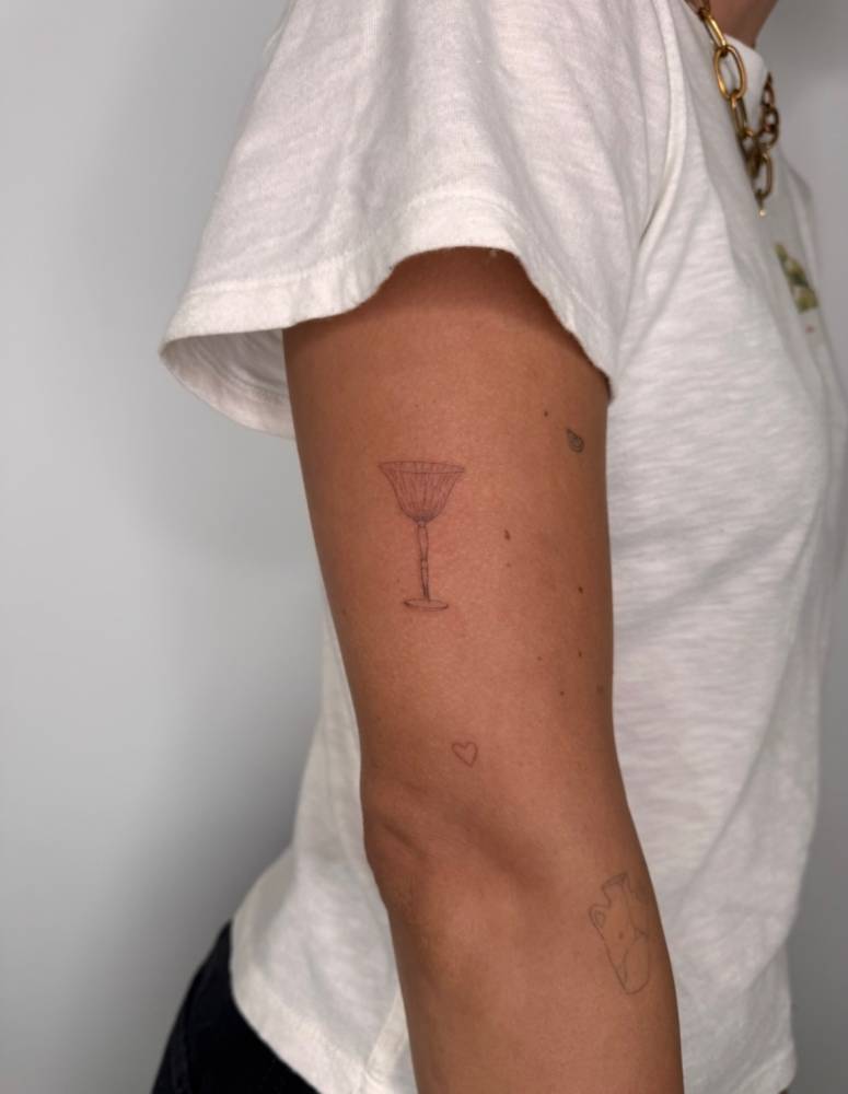 Chalice tattoo located on the upper arm, done in fine line style.