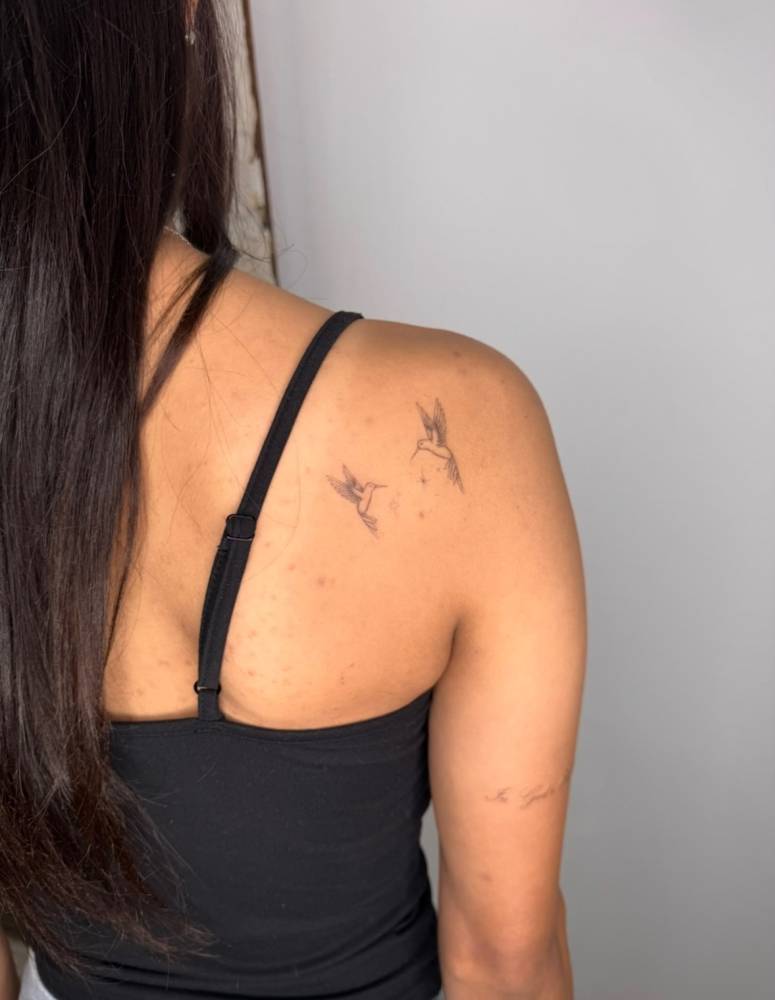 Flying hummingbirds tattooed on the shoulder blade, fine line style.